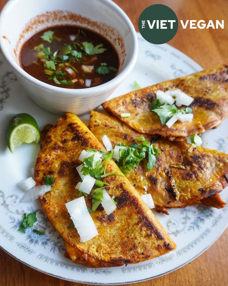 vegan birria tacos with soy curls plated with onion and cilantro with consomme