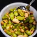 edamame peanut in a soy sauce based dressing in a spoon over a bowl