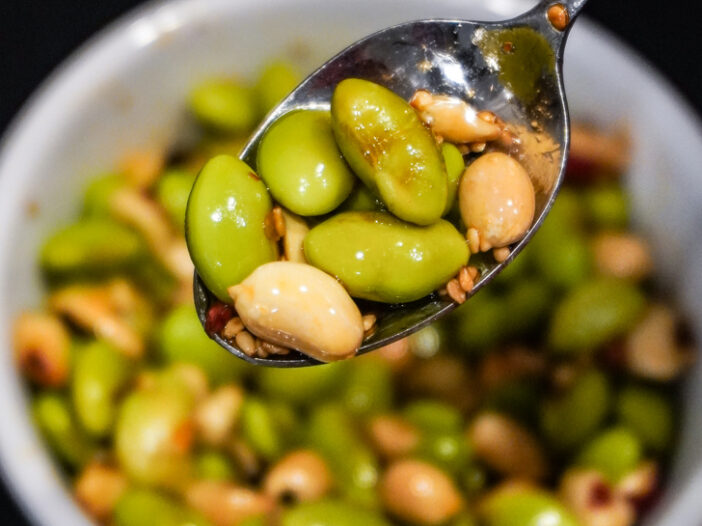 edamame peanut in a soy sauce based dressing in a spoon over a bowl