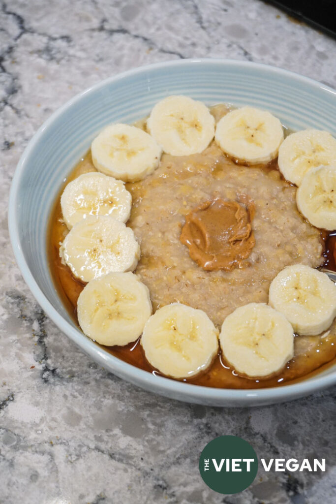 a blue bowl filled with red lentil oats, topped with banana and maple syrup and a dollop of peanut butter in the middle.