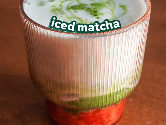 a ribbed pink glass with smashed strawberries and an iced matcha drink