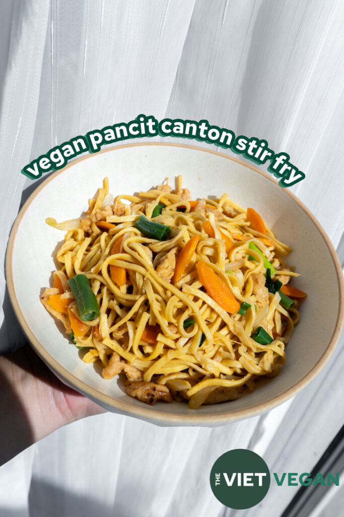 vegan pancit canton stir fry in a white bowl in front of a white sheer curtain